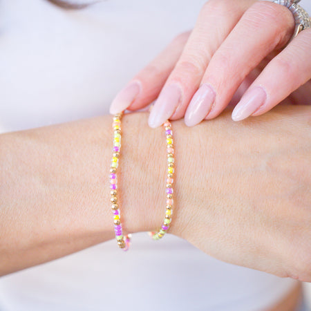 Close-up of a hand wearing a colorful beaded bracelet on a plain background