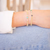 Close-up of a person's wrist wearing two gold bracelets with beads on a blurred background.