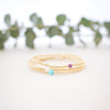 Set of gold bracelets with colorful beads on a white surface with greenery in the background