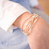 Close-up of a wrist wearing multiple gold beaded bracelets on a blurred background