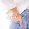 Person wearing a gold bracelet and blue jeans with a blurred background