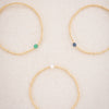 Three gold beaded bracelets with colored beads on a light background