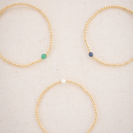 Three gold beaded bracelets with colored beads on a light background