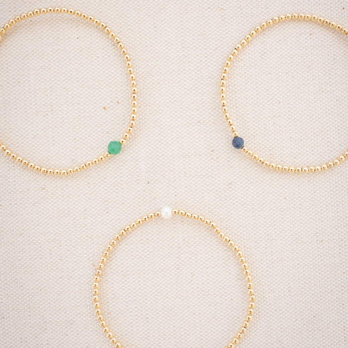 Three gold beaded bracelets with colored beads on a light background
