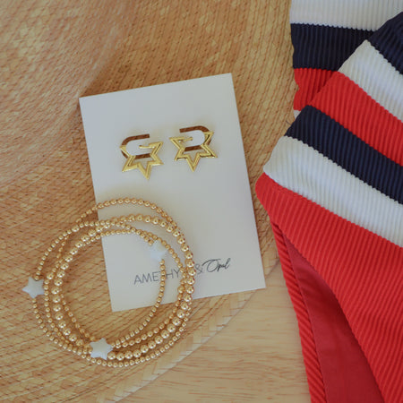 Gold star-shaped earrings on a card with a necklace and striped fabric on a wooden surface