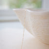 Delicate gold chain necklace draped over a textured white vase with a blurred natural background