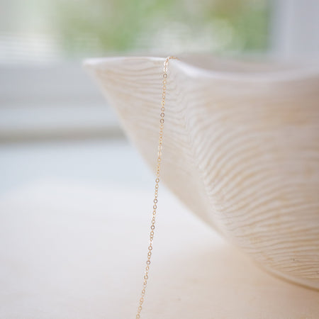 Delicate gold chain necklace draped over a textured white vase with a blurred natural background