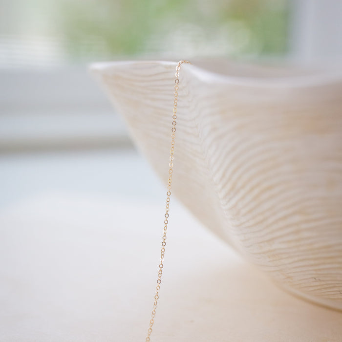 Delicate gold chain necklace draped over a textured white vase with a blurred natural background