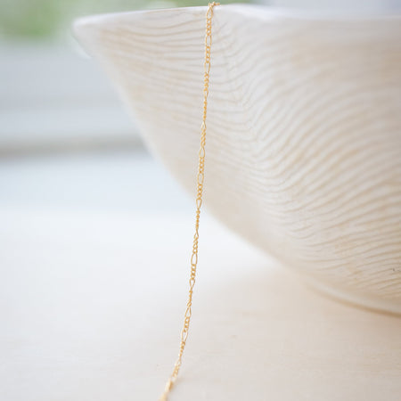 Gold necklace draped over a white ceramic bowl with a blurred background