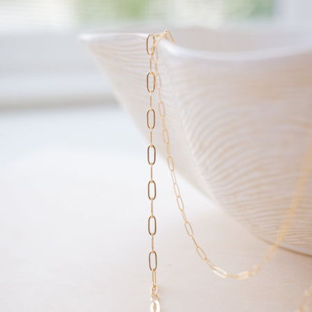 Gold chain necklace on a white surface with a blurred background