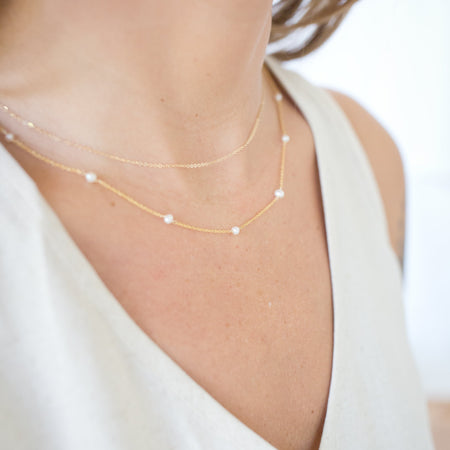 Gold necklace on a person wearing a white top with a blurred background