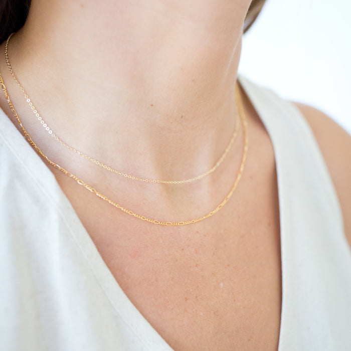 Gold necklace on a person wearing a white top against a neutral background