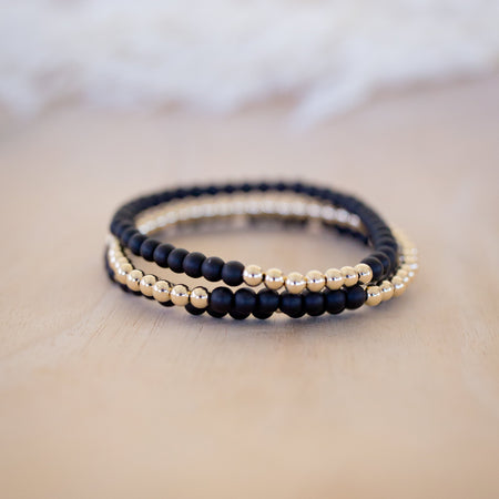 Set of black and gold beaded bracelets on a soft beige surface