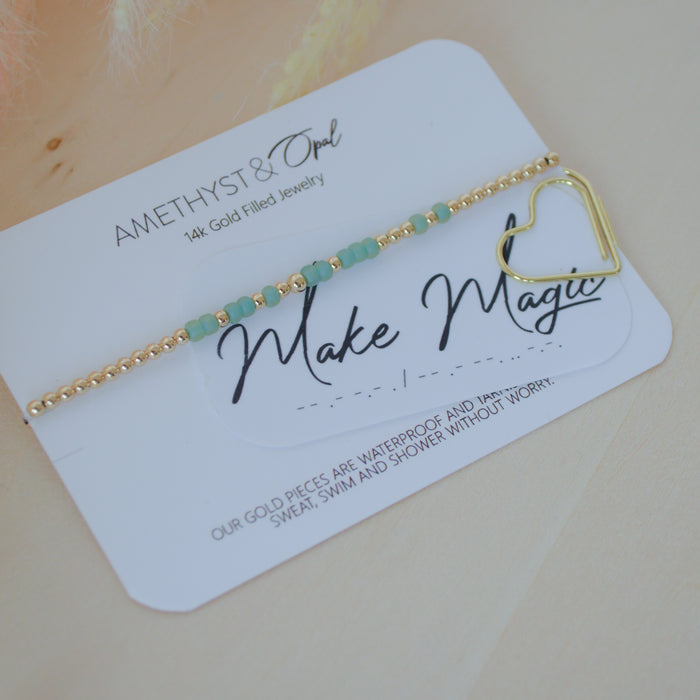 Gold bracelet with heart charm on a 'Make Magic' card by Amethyst & Opal
