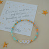Colorful beaded bracelet with letter beads on a beige background with decorative stars and a card.