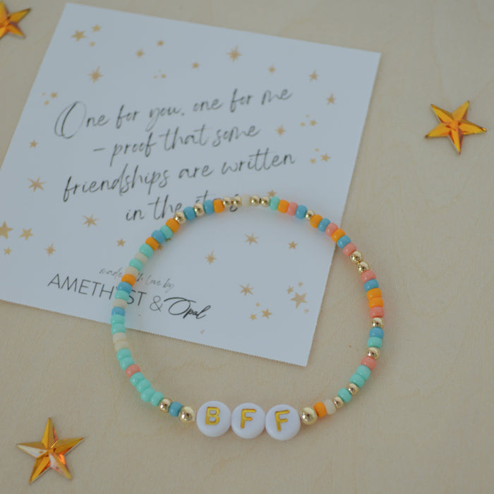 Colorful beaded bracelet with letter beads on a beige background with decorative stars and a card.