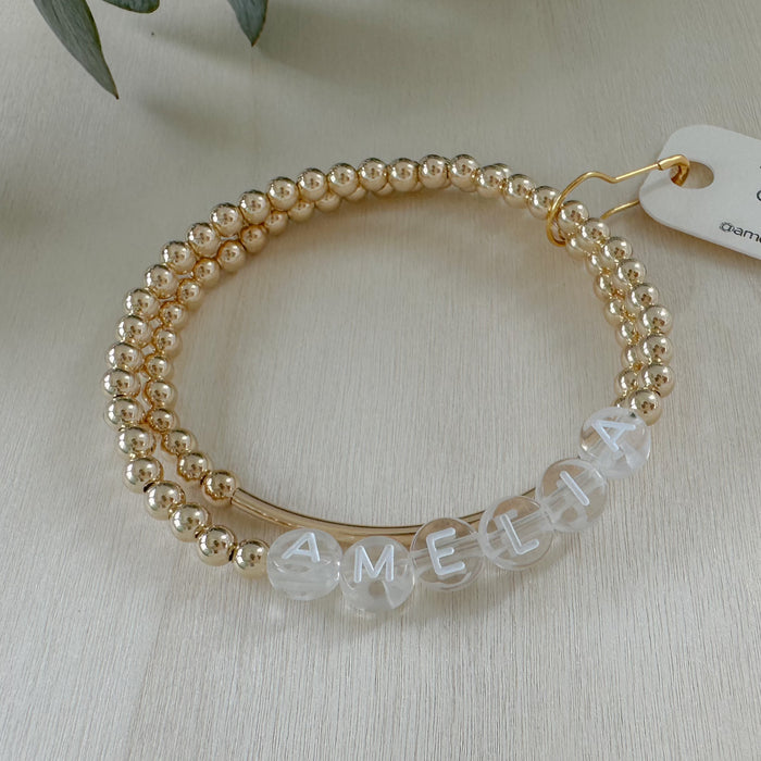 Gold beaded bracelet with clear beads spelling 'AMELIA' on a light background