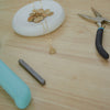 Gold necklace on a white stone with pliers and a blue tool on a wooden surface