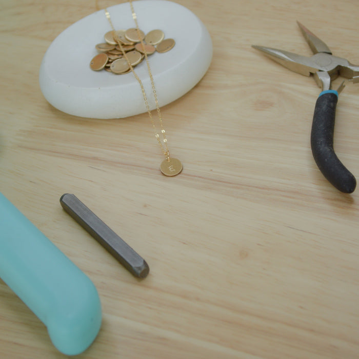 Gold necklace on a white stone with pliers and a blue tool on a wooden surface
