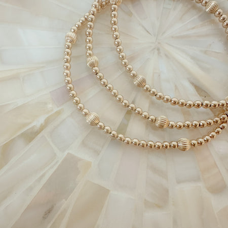 A gold-filled corrugated beaded bracelet with amethyst and opal beads, displayed on a white textured background.