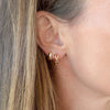 Close-up of an ear wearing gold earrings with blonde hair.