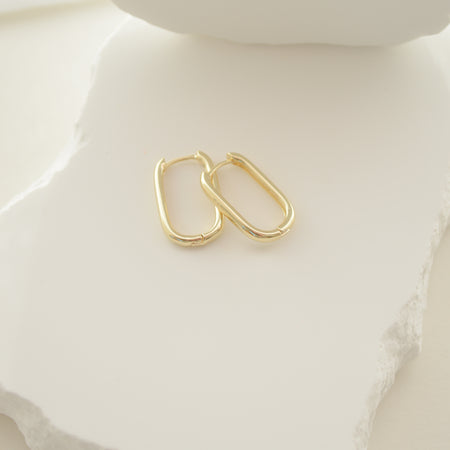Gold hoop earrings on a white ceramic surface