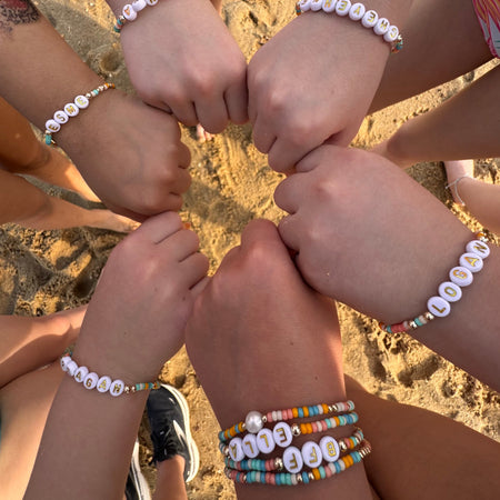 Children's hands wearing beaded bracelets on a beach.