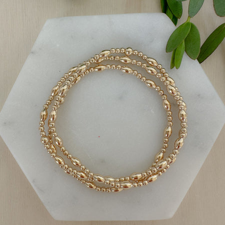A gold-filled bracelet with a mix of rice and round beads, displayed on a marble surface.