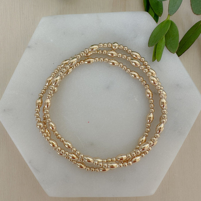 A gold-filled bracelet with a mix of rice and round beads, displayed on a marble surface.