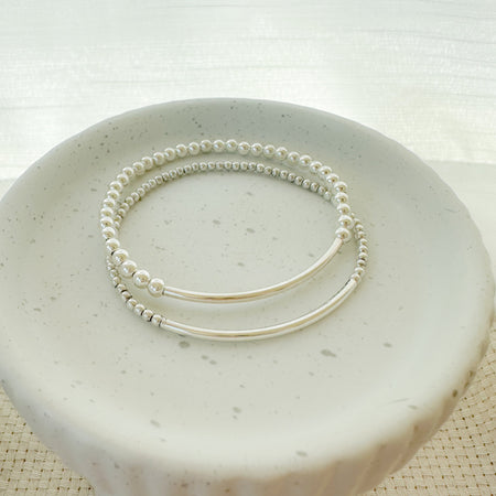 This image features a sleek and elegant Silver Bar Bracelet, showcased on a white, textured surface. The bracelet consists of a sturdy, pre-stretched elastic cord that ensures minimal stretch, maintaining the integrity and style of the piece.