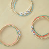 Three beaded bracelets with letter beads on a beige background
