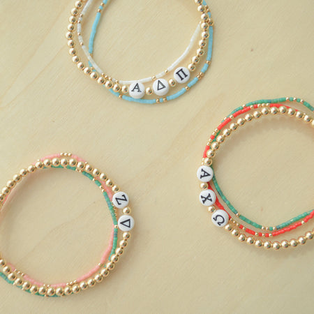 Three beaded bracelets with letter beads on a beige background