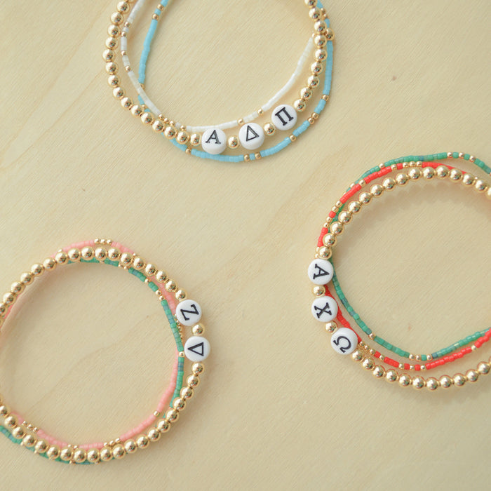 Three beaded bracelets with letter beads on a beige background