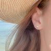 Woman's ear with seashell earrings and sun hat