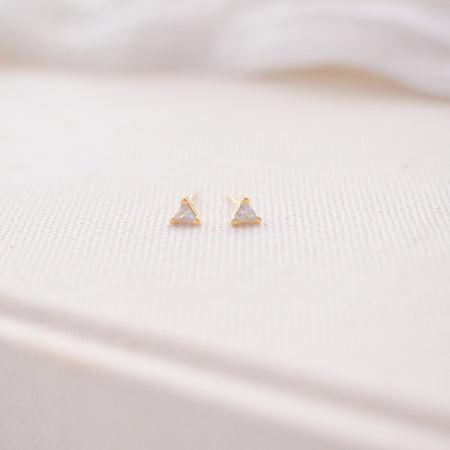 Gold triangle-shaped earrings on a soft pink fabric background