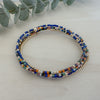 A stack of four bracelets featuring a mix of navy, sage, pumpkin, and brown colors with gold filled beads and delicate seed beadwork on a white wooden surface.