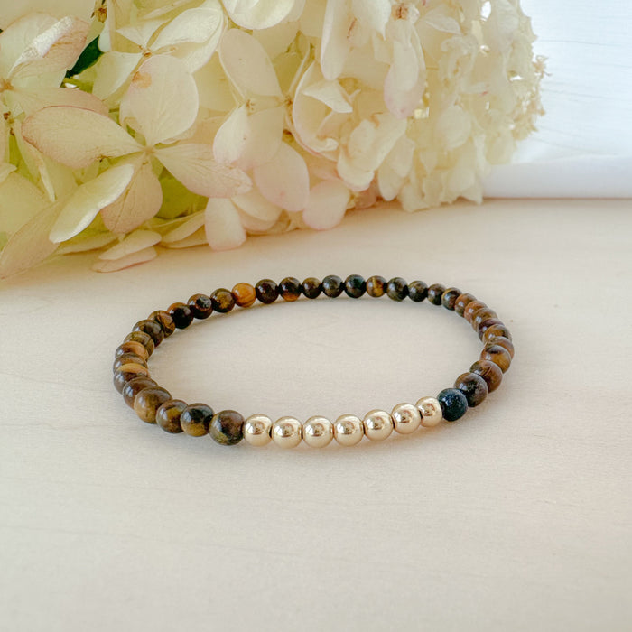 Beaded bracelet with gold and multicolored beads on a light surface with flowers in the background