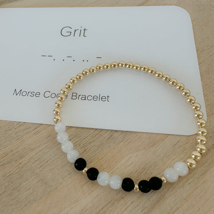 A Morse Code bracelet with the word 'Walk' written above it, featuring 14k gold filled beads and clear gemstone beads on a wooden surface.