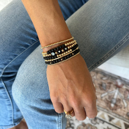 A person wearing a stack of gold-filled onyx bead bracelets on their wrist, with black and gold colors predominating.