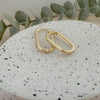 A pair of gold-filled link hoop earrings on a textured white stone with a green leaf in the background.