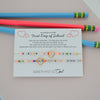 Two colorful beaded friendship bracelets with gold heart charms, presented on a white gift card with school-themed text and decorated with two pencils on a light pink background.