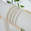 Silver beaded bracelets on a white surface with green leaves in the background